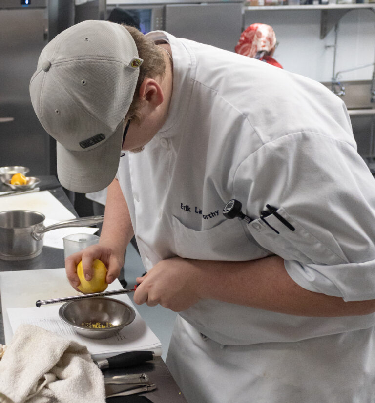 Culinary student finishing dessert with careful detail in the Nossi kitchen.